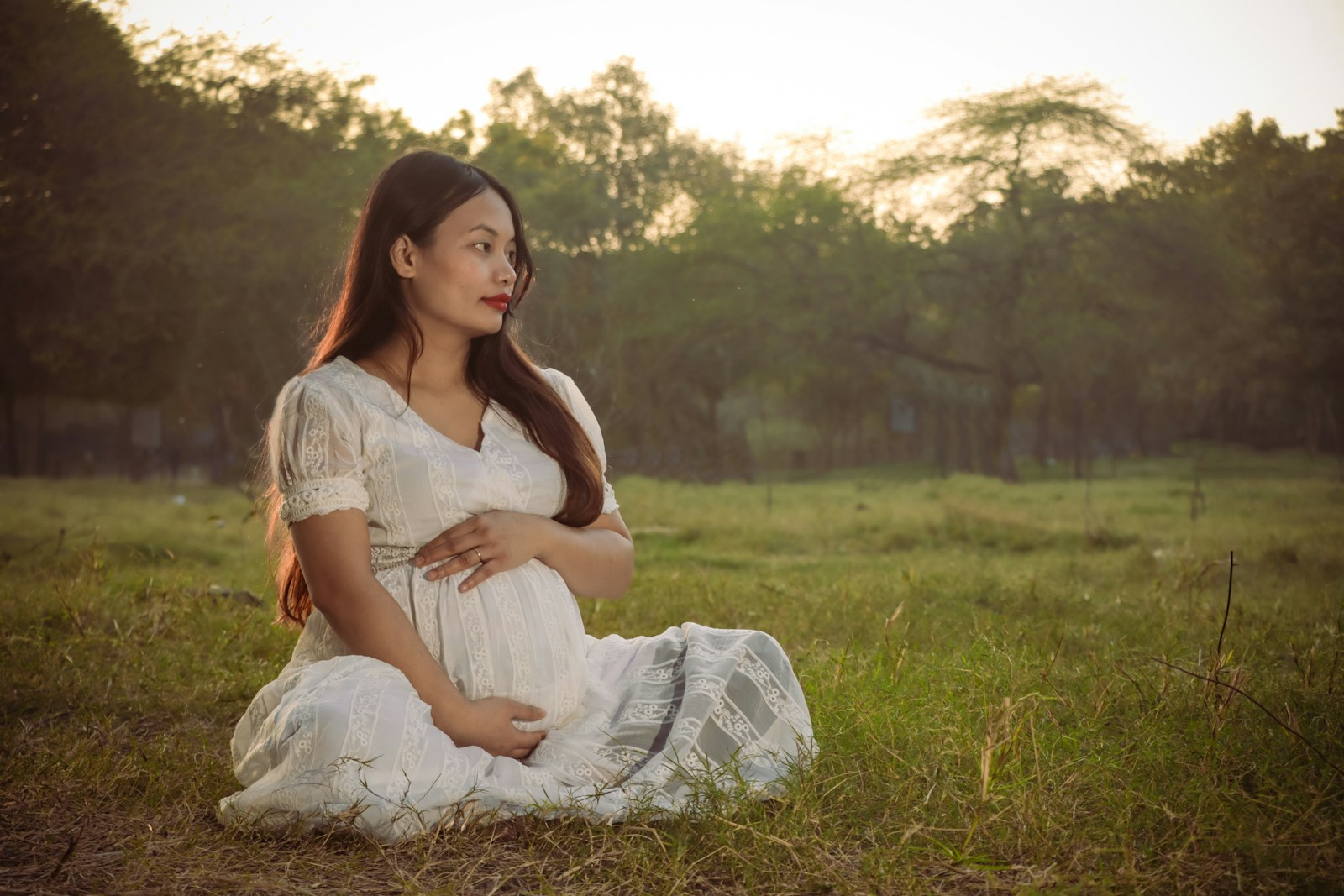 A pregnant woman sitting in a field at sunset
